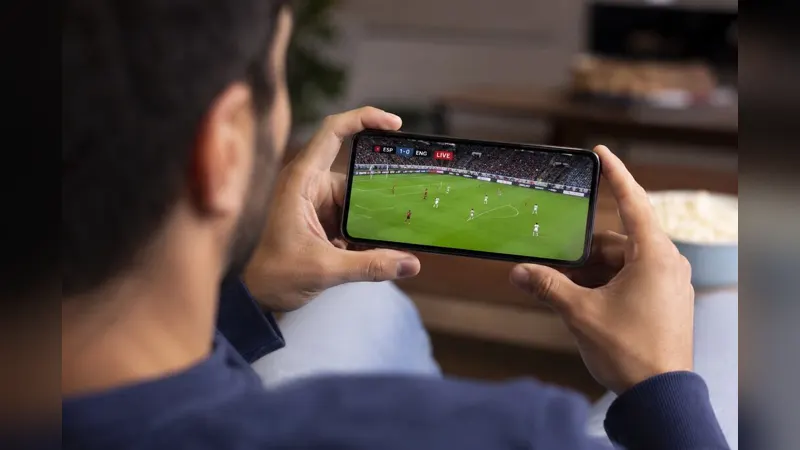 A fan holding a phone horizontally, watching a live football match on the screen