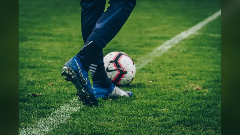A player's feet and boots dribbling a football on the grass
