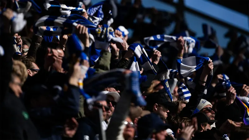 A dense crowd of football fans with scarves in a dark stand