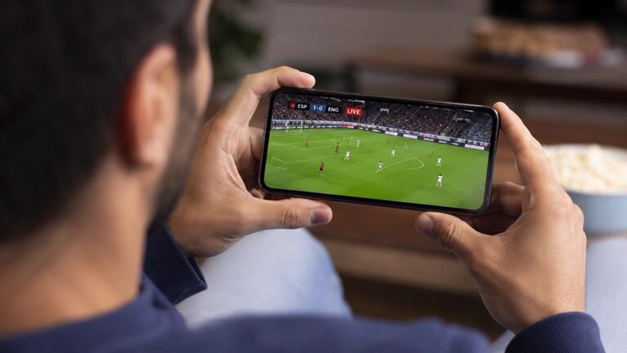 A football fan watching a live match on a smartphone held in both hands